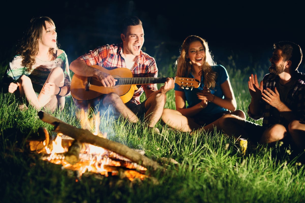 Friends playing guitar gathered around campfire.