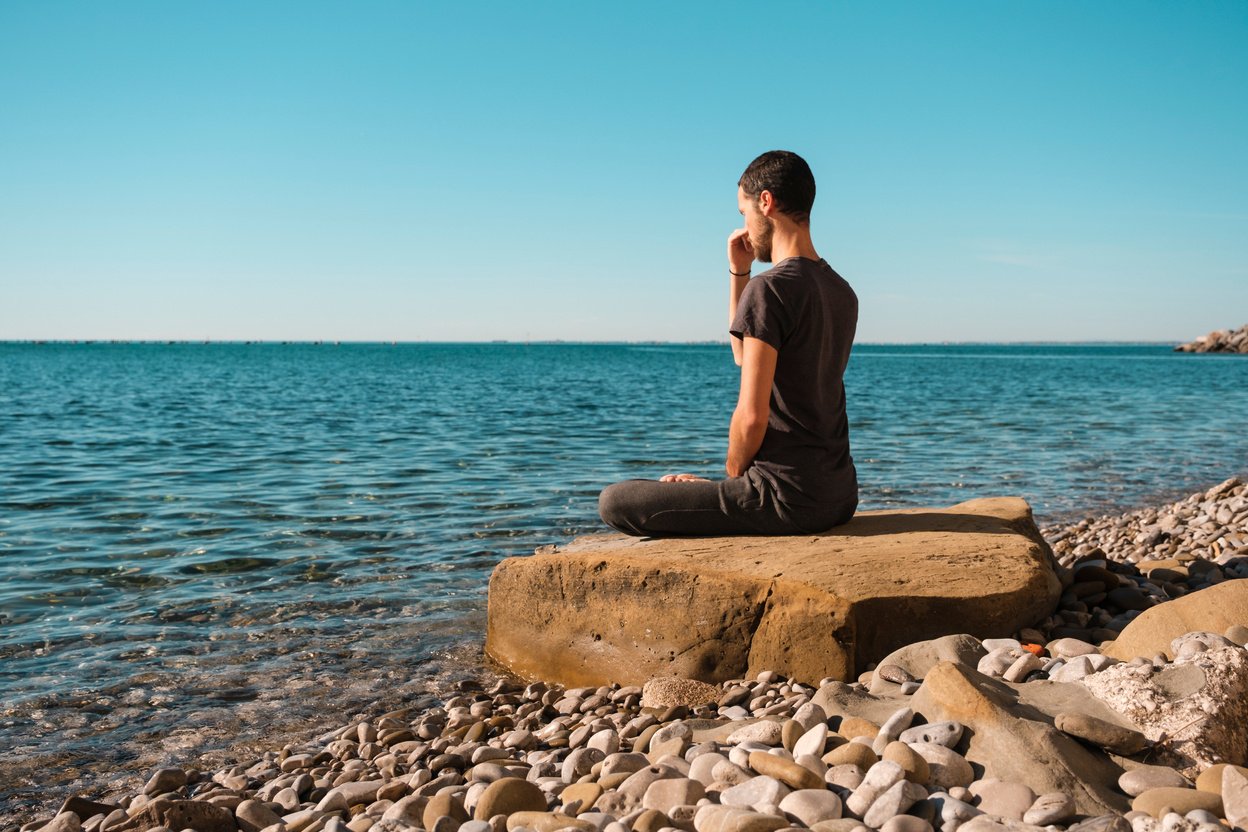 Attractive young man practicing yoga meditation and breathwork outdoors by the sea